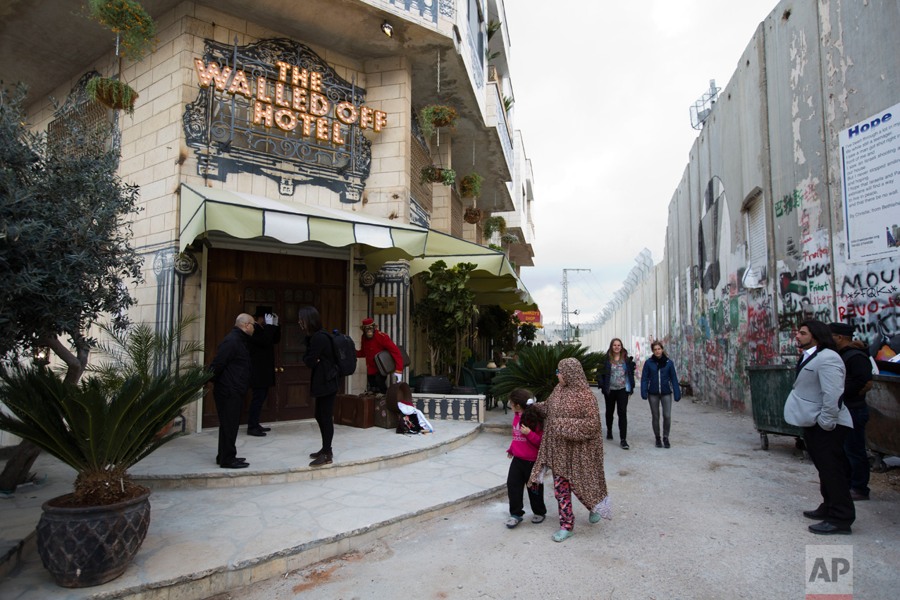  People pass by the "The Walled Off Hotel" and the Israeli security barrier in the West Bank city of Bethlehem, Friday, March 3, 2017. The owner of a guest house packed with the elusive artist Banksy's work has opened the doors of his West Bank establishments to media, showcasing its unique "worst view in the world." The nine-room hotel named "The Walled Off Hotel" will officially open on March 11. (AP Photo/Dusan Vranic) 