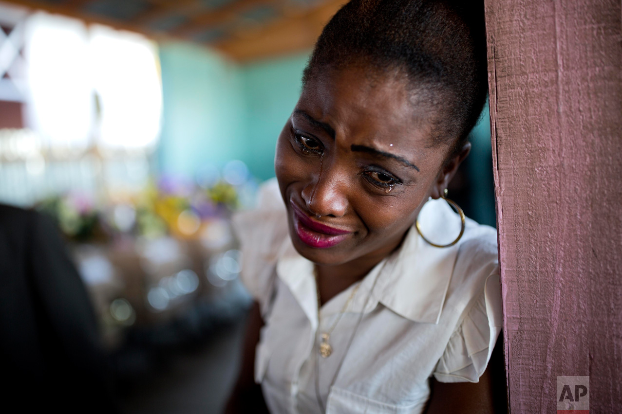 A woman cries near the coffin containing the body of a relative who died at the country's largest prison in Port-au-Prince, Haiti, Tuesday Feb. 21, 2017. Relatives wailed in grief or stared stoically as flowers were placed on 20 caskets at a mass funeral for the latest group of inmates who died miserably in Haiti's largest prison, most without ever having been convicted of any crime. (AP Photo/Dieu Nalio Chery)