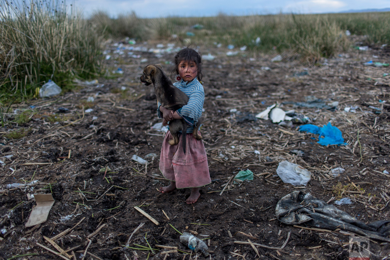 In this Feb. 4, 2017 photo, Melinda Quispe walks on the trash strewn shore of Lake Titicaca, as she holds her dog, in her village Kapi Cruz Grande, in the Puno region of Peru. The governments of Peru and Bolivia signed a pact in January to spend more than $500 million to attack the pollution problem of Lake Titicaca, though the details were vague. (AP Photo/Rodrigo Abd)