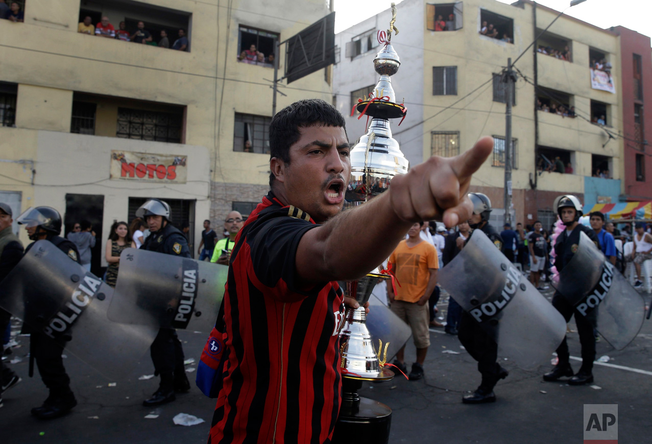 In this Monday, May 1, 2017 photo, a fan of the "Purito Barrios Altos" soccer team yells at rival fans who don't agree with the referee's decision as he runs with his team's trophy after the Little World Cup of Provenir street soccer championship in Lima, Peru. All 56 teams bring their fans to defend each goal, even if it comes to blows, so about 50 anti-riot police line the pitch. (AP Photo/Martin Mejia) 