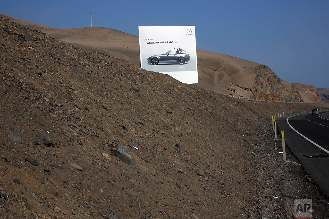 In this May 5, 2017 photo, a billboard advertising a Mazda sports car stands along the Pan American Highway on the south side of Lima, Peru. Standing on the brown, barren landscape, the billboards advertise other products the people living in this area are unlikely to be able to buy or afford. (AP Photo/Rodrigo Abd)
