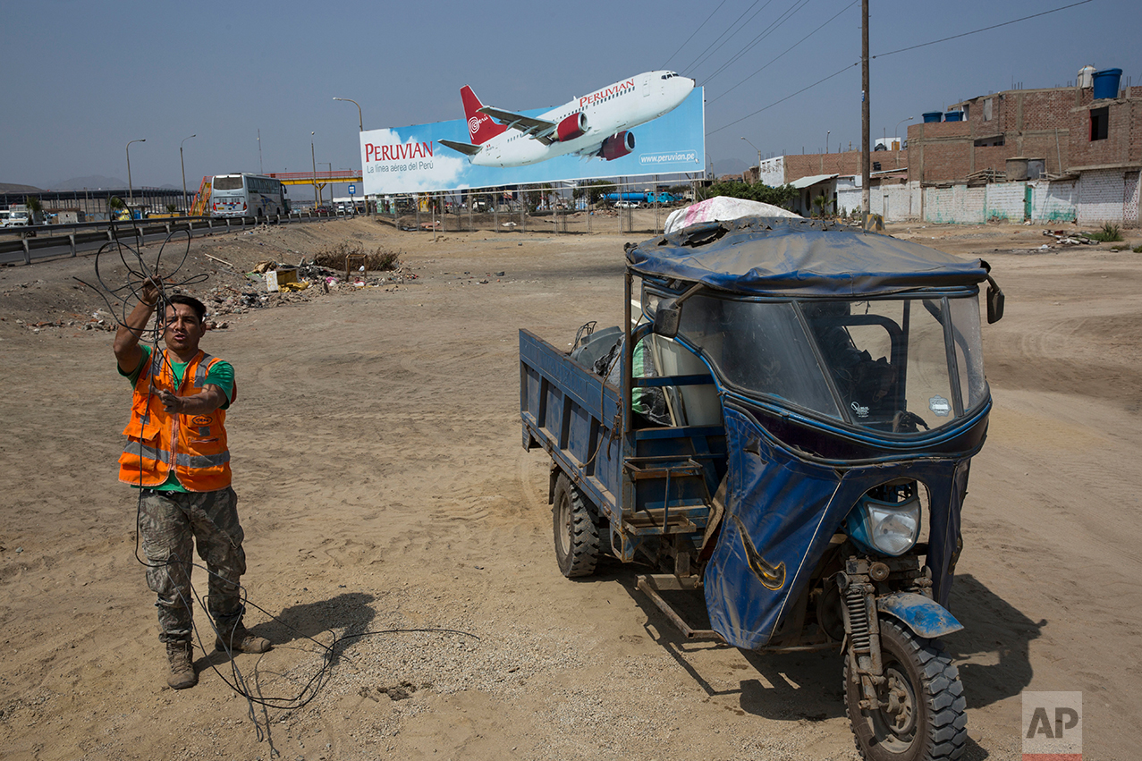 In this May 5, 2017 photo, a man collects cables for resale, along with other recyclable objects, along the Pan American Highway where a billboard advertises a local airline on the south side of Lima, Peru. Below the billboards are cannibalized cars, piles of used brick and white crosses marking the places where people died along the highway. (AP Photo/Rodrigo Abd)