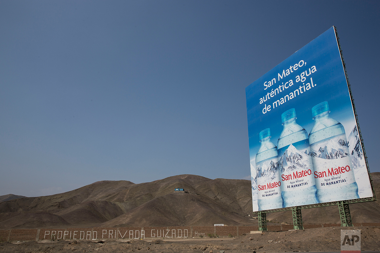 In this May 5, 2017 photo, a billboard advertising spring water stands along the Pan American Highway on the south side of Lima, Peru. Trash is scattered around the area where people live in homes without potable water and adequate public services, menaced by local gangs that invade and traffic in properties. (AP Photo/Rodrigo Abd)