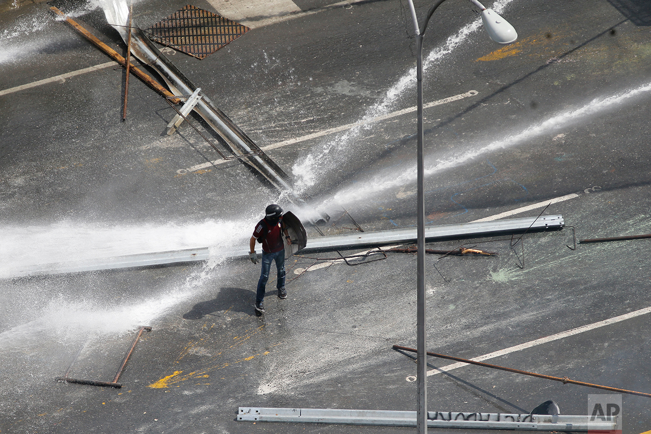 A protester walks between two water canons sprayed by security forces to block an opposition march from reaching the Ombudsman's Office, as the opposition protests President Nicolas Maduro in Caracas, Venezuela, on Monday, May 29, 2017. Protests against Maduro's government have left dozens dead in the past two months. The opposition wants immediate presidential elections and the freeing of political prisoners. (AP Photo/Ariana Cubillos)