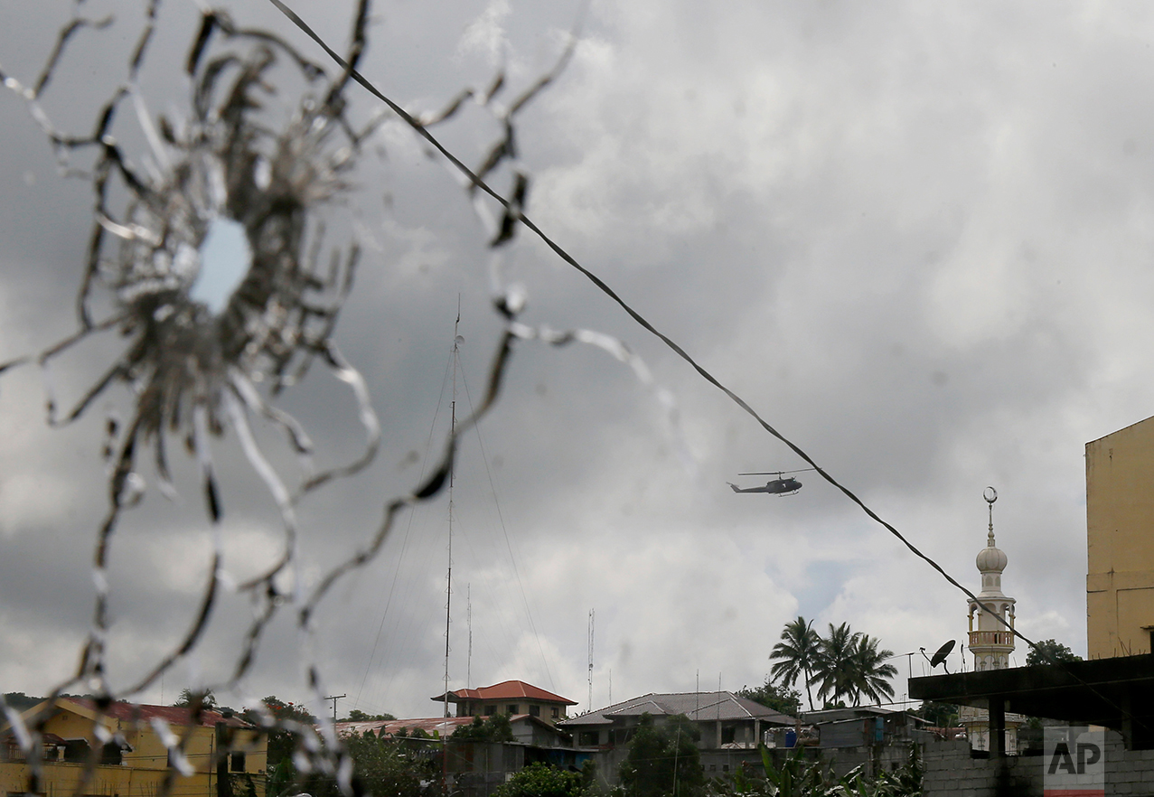 A military helicopter hovering by a mosque is seen through shattered glass after fighting between government troops and Muslim militants who continue to hold their ground in some areas of Marawi city for almost a week Monday, May 29, 2017 in the southern Philippines. Philippine forces control most of the city where militants linked to the Islamic State group launched a bloody siege nearly a week earlier, authorities said Monday, as the army launched airstrikes and went house-to-house to search for resistance. (AP Photo/Bullit Marquez)