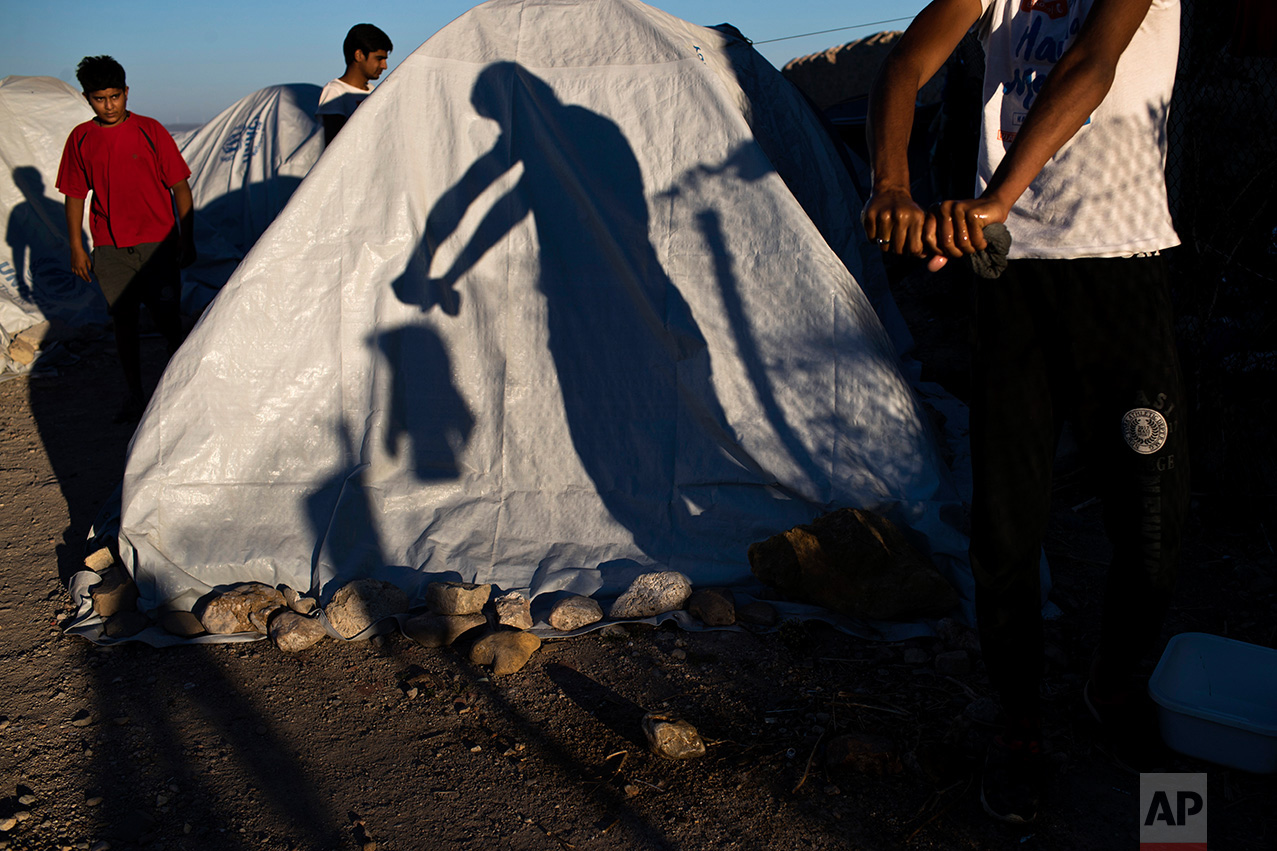 In this June 9, 2017 photo, a Pakistani migrant wrings a t-shirt as his shadow falls on a tent at a beach near the Souda refugee camp, where hundreds refugees and other migrants live in makeshift tents on Chios island, Greece. (AP Photo/Petros Giannakouris)