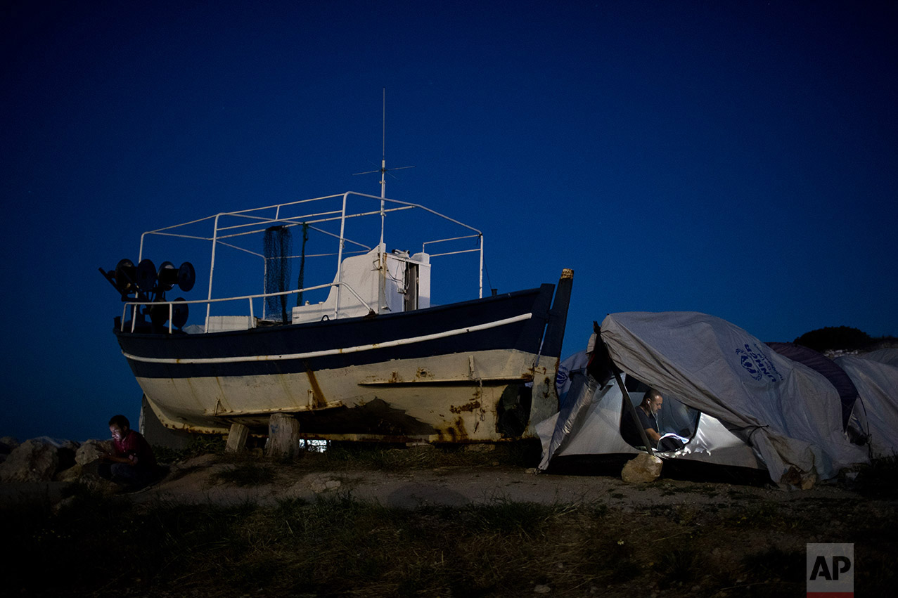 In this June 9, 2017 photo, a refugee chats with his phone inside his shelter that stands next to a fishing boat near the Souda refugee camp, on Chios island, Greece. (AP Photo/Petros Giannakouris)