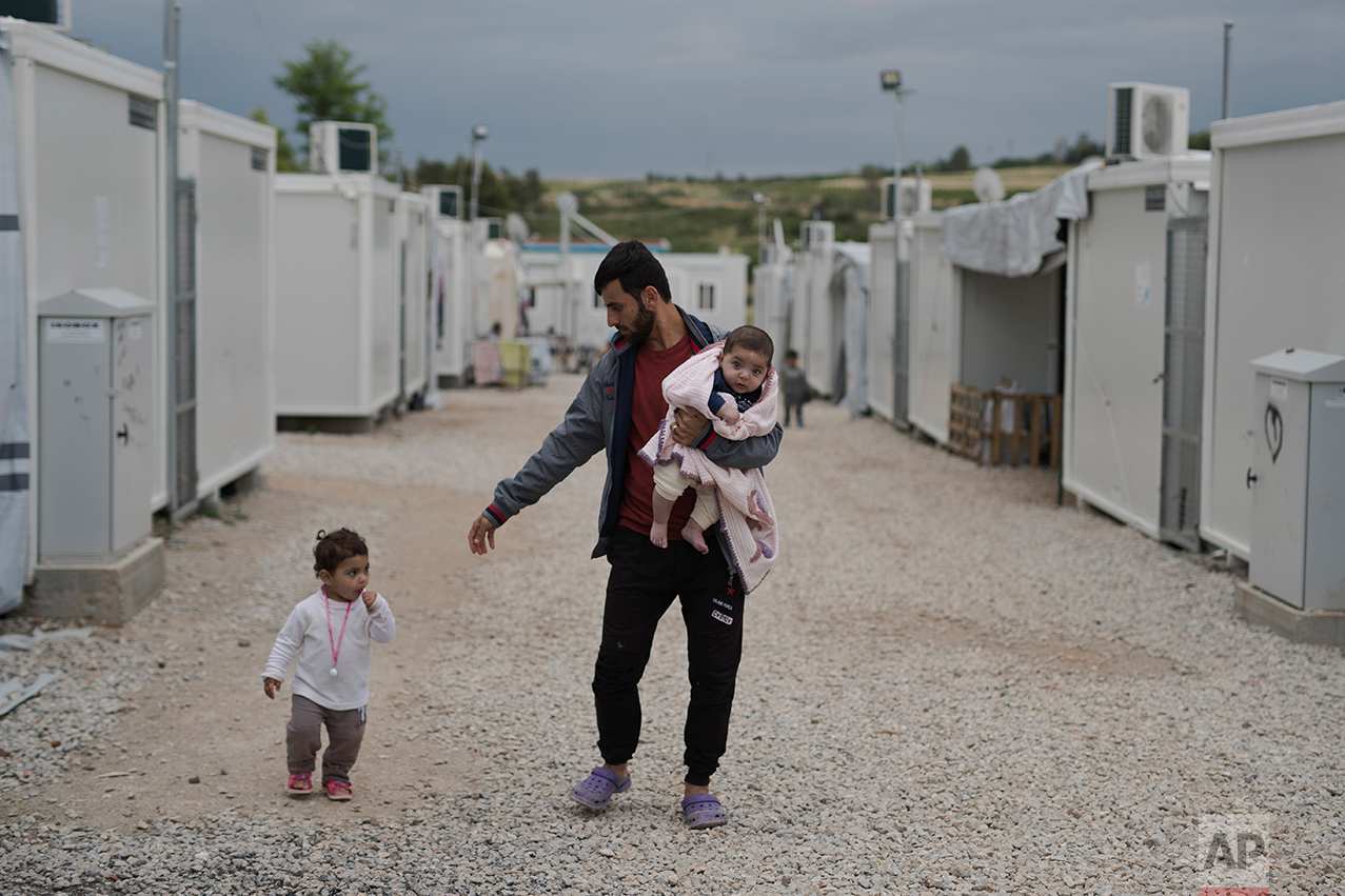In this May 29, 2017 photo, Barzan Hasan from Irbil, Syria, holds his 5-month-old baby girl Gaylan, as he walks next to his other daughter Lamar on their way to their shelter at the refugee camp of Ritsona about 86 kilometers (53 miles) north of Athens. The family has been stuck in Greece for almost one year and a half, Gaylan was born as a refugee in Greece. (AP Photo/Petros Giannakouris)
