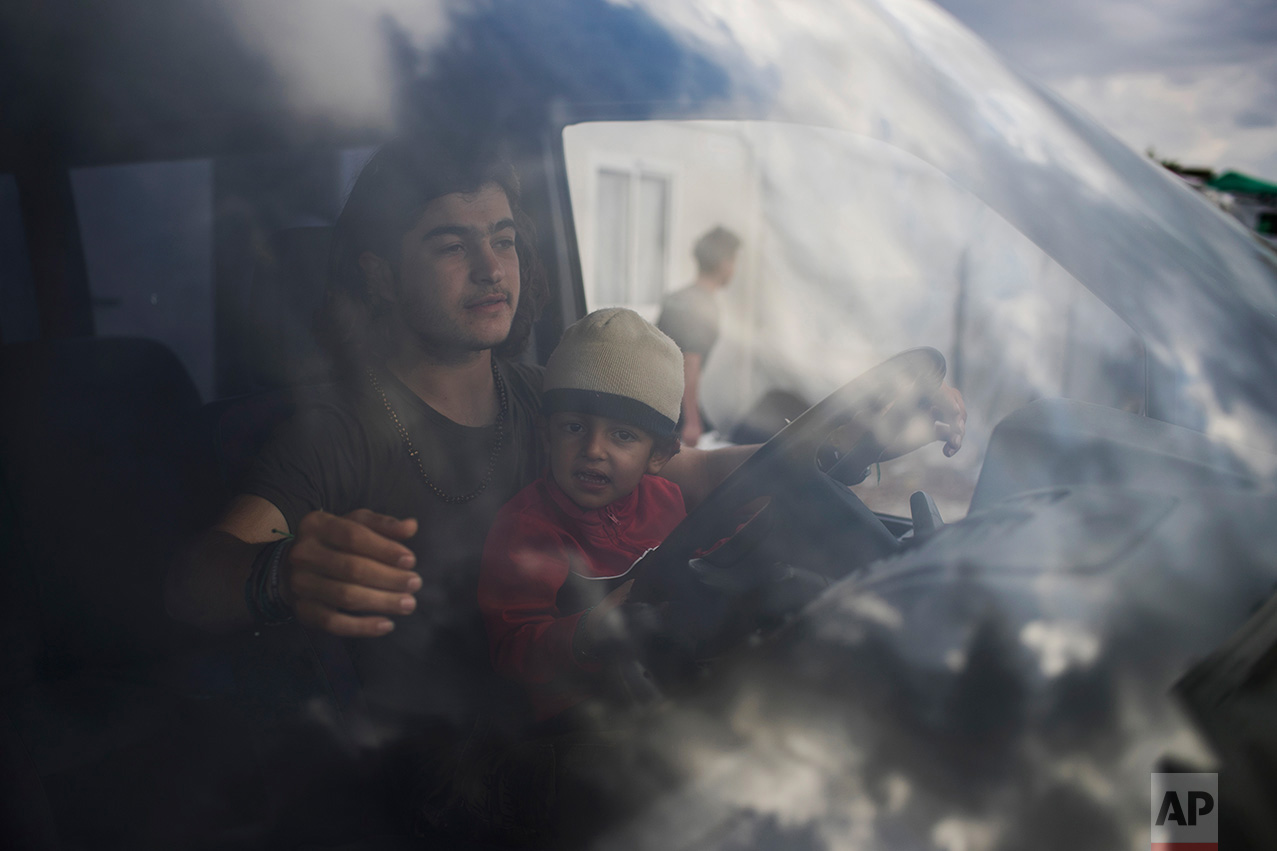 In this May 26, 2017 photo, a Syrian man with a boy drives a van as he distributes food inside the refugee camp of Ritsona about 86 kilometers (53 miles) north of Athens. (AP Photo/Petros Giannakouris)