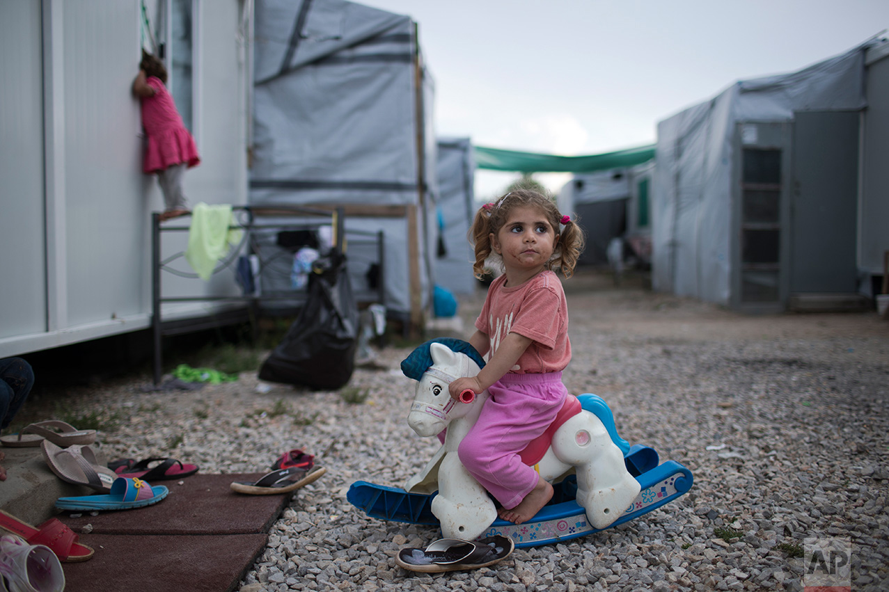 In this May 25, 2017 photo, three-year-old Ragika from Syria plays with a plastic toy horse at the refugee camp of Ritsona about 86 kilometers (53 miles) north of Athens. According to the UN Refugee agency there are more than 21 millions refugees around the world. (AP Photo/Petros Giannakouris)