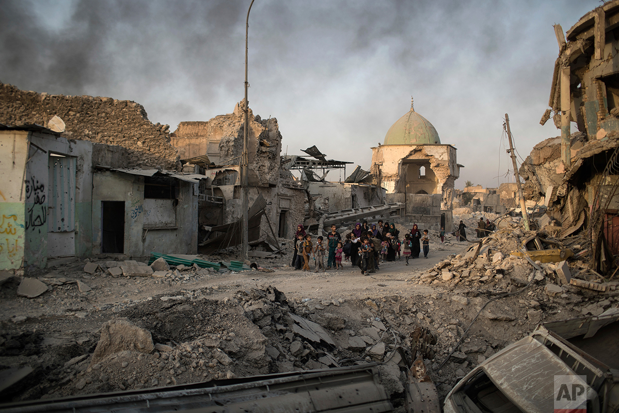 Fleeing Iraqi civilians walk past the heavily damaged al-Nuri mosque as smoke rises in the background in the Old City of Mosul, Iraq, Tuesday, July 4, 2017. As Iraqi forces continued to advance on the last few hundred square kilometers of Mosul held by the Islamic State group, the country's Prime Minister said Tuesday the gains show Iraqis reject terrorism. (AP Photo/Felipe Dana)