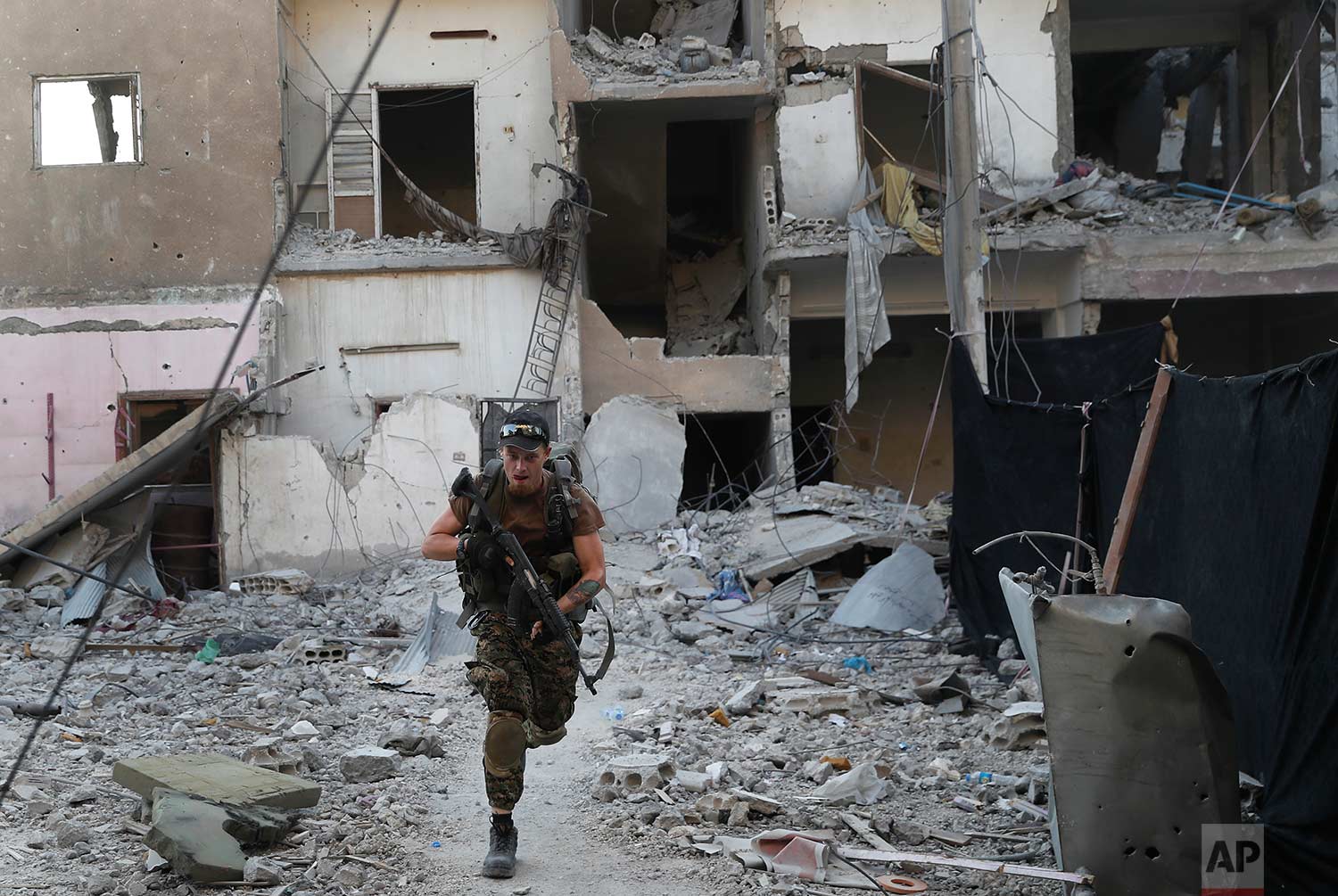 A U.S.-backed Syrian Democratic Forces fighter runs in front of a damaged building as he crosses a street on the front line, in Raqqa city, Syria, Thursday, July 27, 2017. (AP Photo/Hussein Malla)