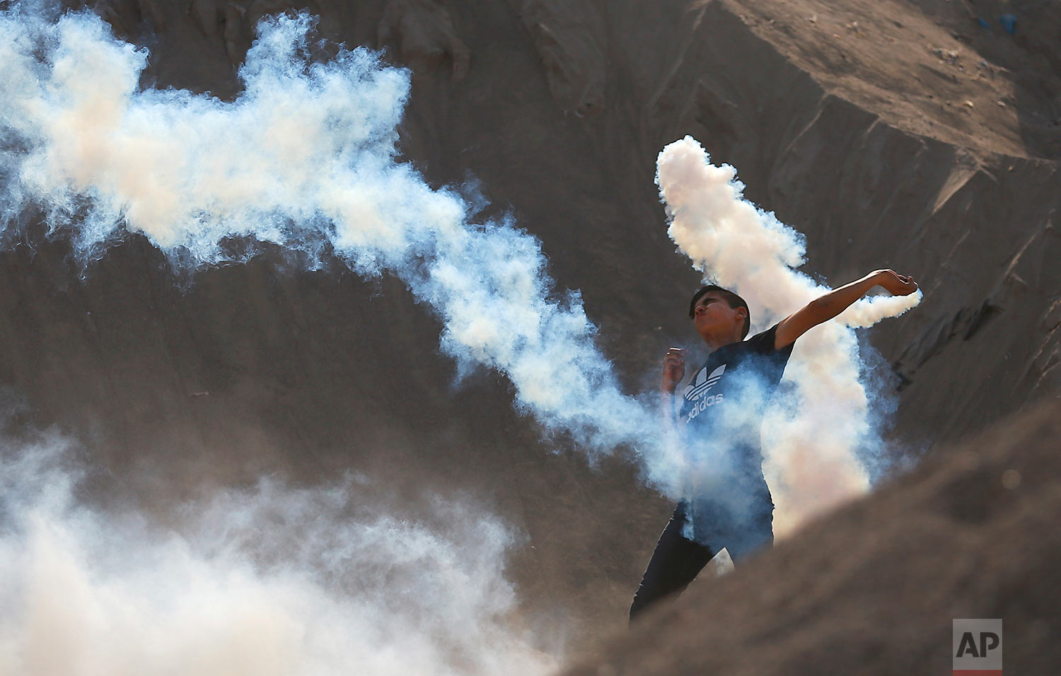 A Palestinian protester throws a teargas canister fired by Israeli soldiers back during clashes on the Israeli border with Gaza, Friday, July 21, 2017. (AP Photo/Khalil Hamra)