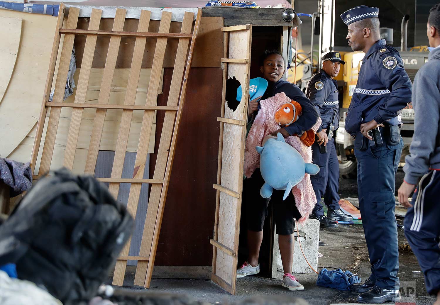 A police officer stands by as a woman carries her belongings during an eviction of people living in shacks beneath an overpass, in Sao Paulo, Brazil, Saturday, July 29, 2017. (AP Photo/Andre Penner)
