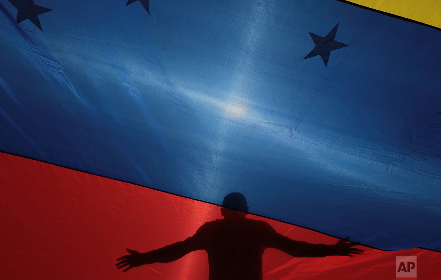 The silhouette of an anti-government protester is seen through a Venezuelan flag during a call by the opposition to block roads for 10 hours in Caracas, Venezuela, Monday, July 10, 2017. (AP Photo/Fernando Llano)