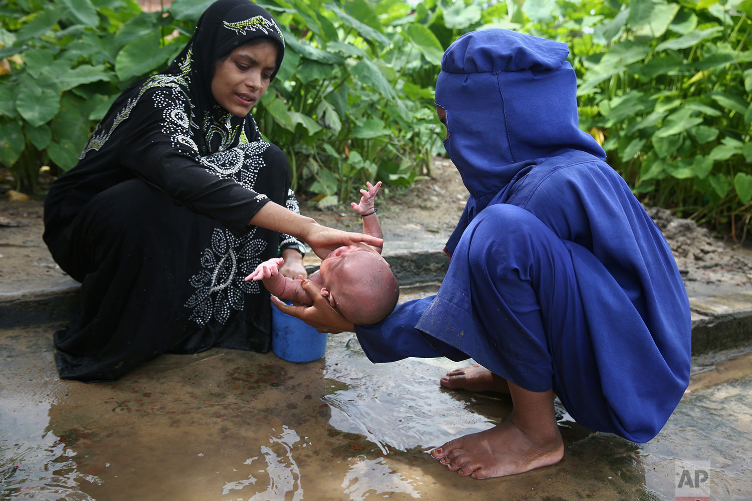 Myanmar's Rohingya Muslim ethnic minority women bathe a week-old infant at the Kutupalong makeshift refugee camp in Cox's Bazar, Bangladesh, Wednesday, Aug. 30, 2017. Thousands of Rohingya Muslims have fled fresh violence in Myanmar and crossed into Bangladesh in less than a week, with hundreds stranded in no man's land at the countries' border, the International Organization for Migration said Wednesday. (AP Photo/Mushfiqul Alam)