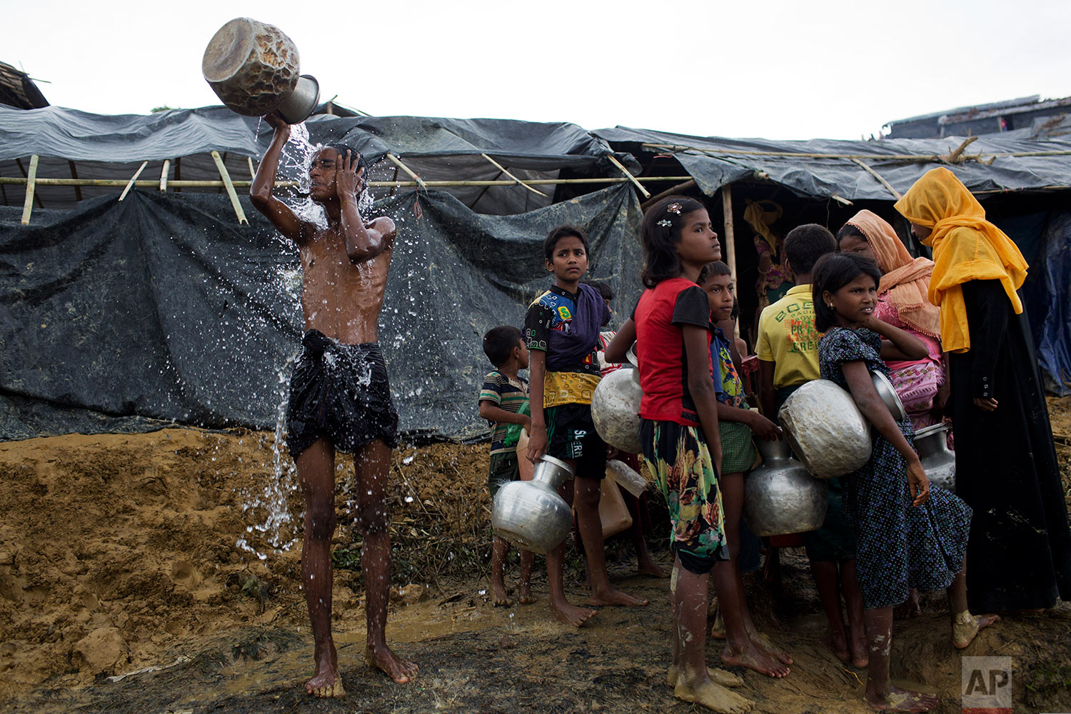 Newly arrived Rohingya wait to collect water from a tube well that was installed a few days ago, as a boy bathes beside them, at Ukhia, Bangladesh, Saturday, Sept. 9, 2017. (AP Photo/Bernat Armangue)
