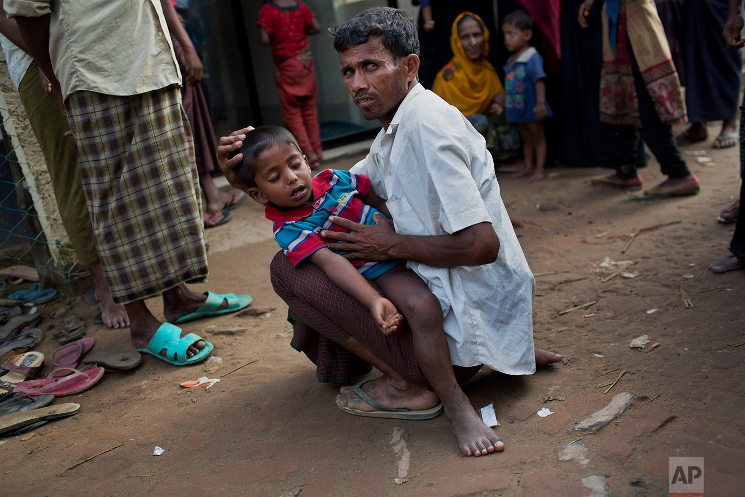 A Rohingya Muslim man holds a child with feveras they await treatment outside a clinic at Leda Refugee Camp, Bangladesh, Saturday, Sept. 9, 2017. (AP Photo/Bernat Armangue)