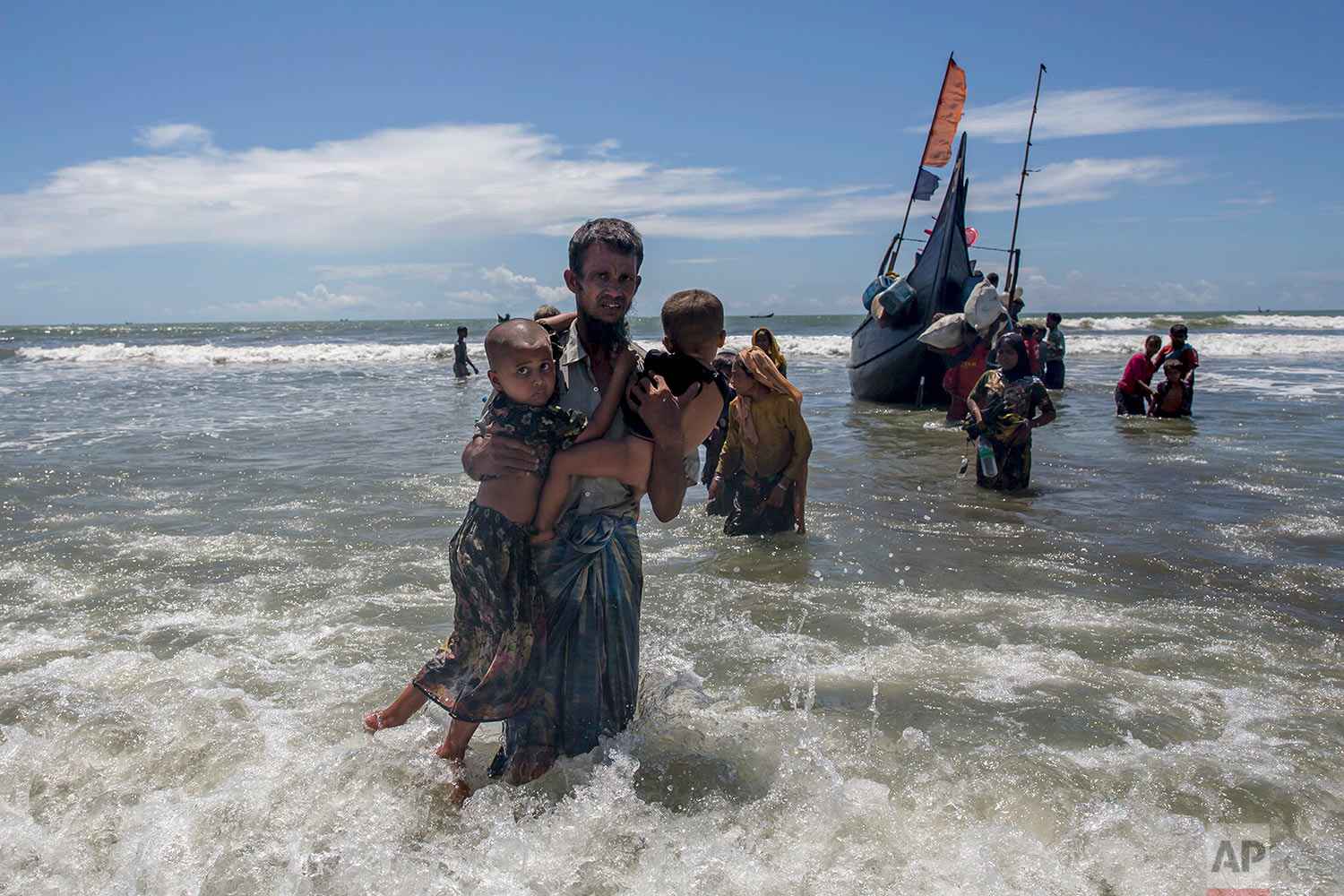 A Rohingya Muslim man walks to shore carrying two children after they arrived on a boat from Myanmar to Bangladesh in Shah Porir Dwip, Bangladesh, Thursday, Sept. 14, 2017. Those who arrived Wednesday in wooden boats described ongoing violence in Myanmar, where smoke could be seen billowing from a burning village, suggesting more Rohingya homes had been set alight. (AP Photo/Dar Yasin)