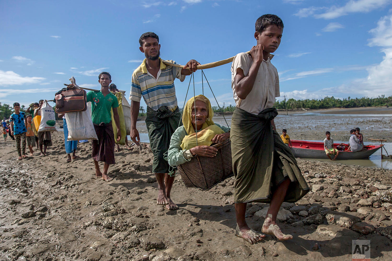 Rohingya Muslims, who crossed over from Myanmar into Bangladesh, carry an elderly woman in a basket and walk towards a refugee camp in Shah Porir Dwip, Bangladesh, Thursday, Sept. 14, 2017. Nearly three weeks into a mass exodus of  (AP Photo/Dar Yasin)