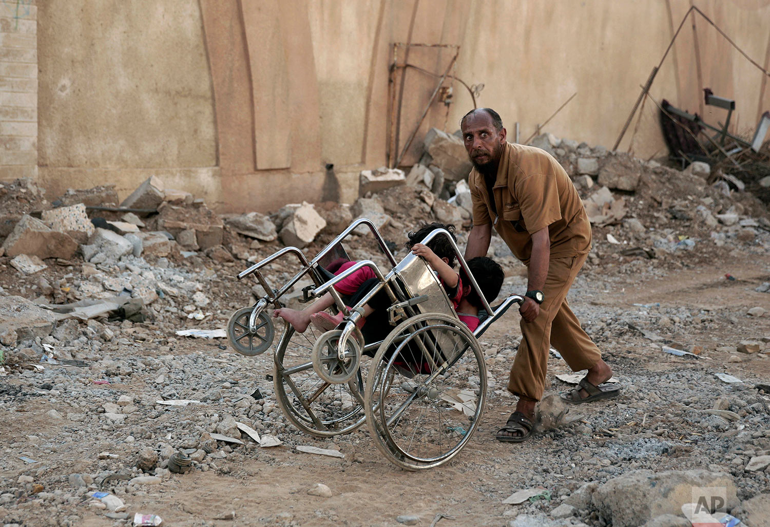  A man pushes two children in a wheelchair as they flee heavy fighting between Islamic State militants and Iraqi special forces in Mosul, Iraq, Wednesday, May 10, 2017. (AP Photo/Maya Alleruzzo) 