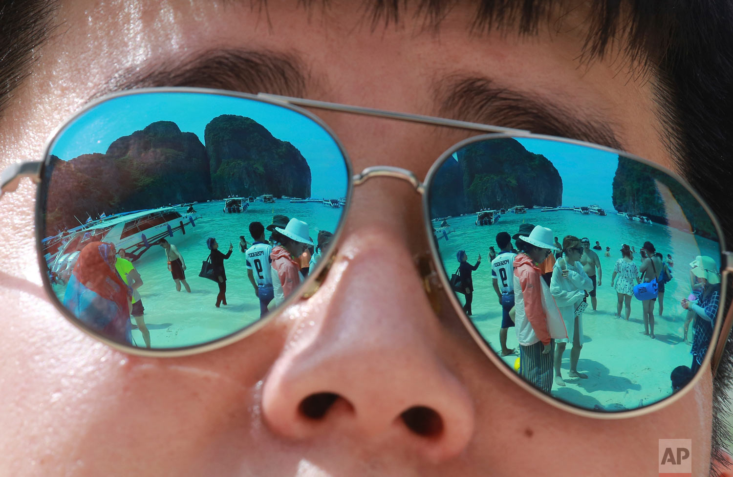  In this Thursday, May 31, 2018, photo tourists are reflected in sunglasses on Maya Bay on Phi Phi island in Krabi province, Thailand. Maya Bay on Phi Phi Leh Island in the Andaman Sea will close to tourists for four months from Friday to give its coral reefs and sea life a chance to recover from an onslaught that began nearly two decades ago. (AP Photo/Sakchai Lalit) 
