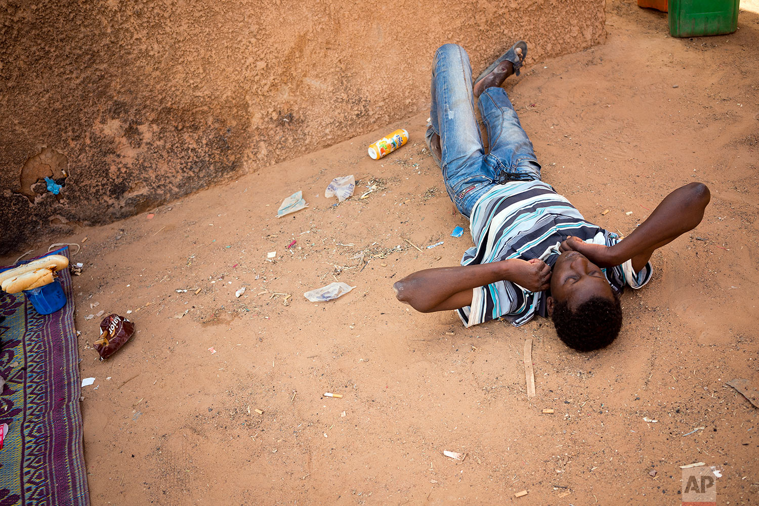  A young migrant who has been expelled from Algeria lays after being restrained by others after he attempted to strip naked in a transit center in Arlit, Niger, on June 2, 2018. (AP Photo/Jerome Delay) 