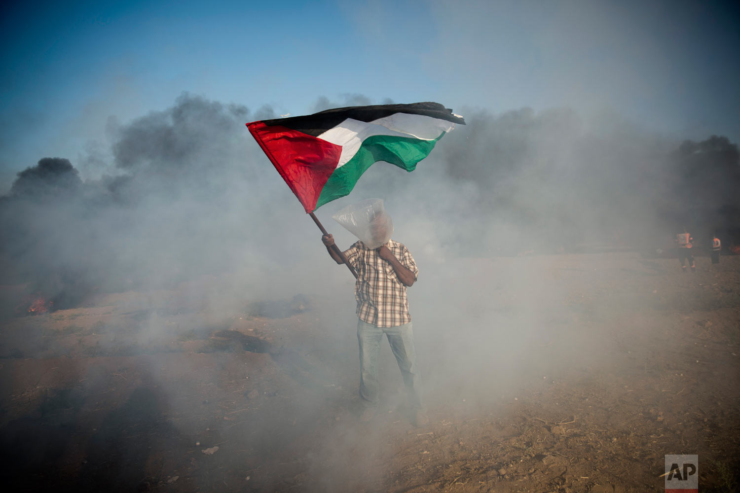  A Palestinian protester wears a plastic bag on his head as a protection from teargas as he waves a national flag during a protest at the Gaza Strip's border with Israel, Friday, Aug.10, 2018. Violence erupted at the Gaza border Friday after the territory's militant Islamic Hamas rulers and Israel appeared to be honoring a cease-fire that ended two days of intense violence amid efforts by neighboring Egypt to negotiate between the two sides. (AP Photo/Khalil Hamra) 