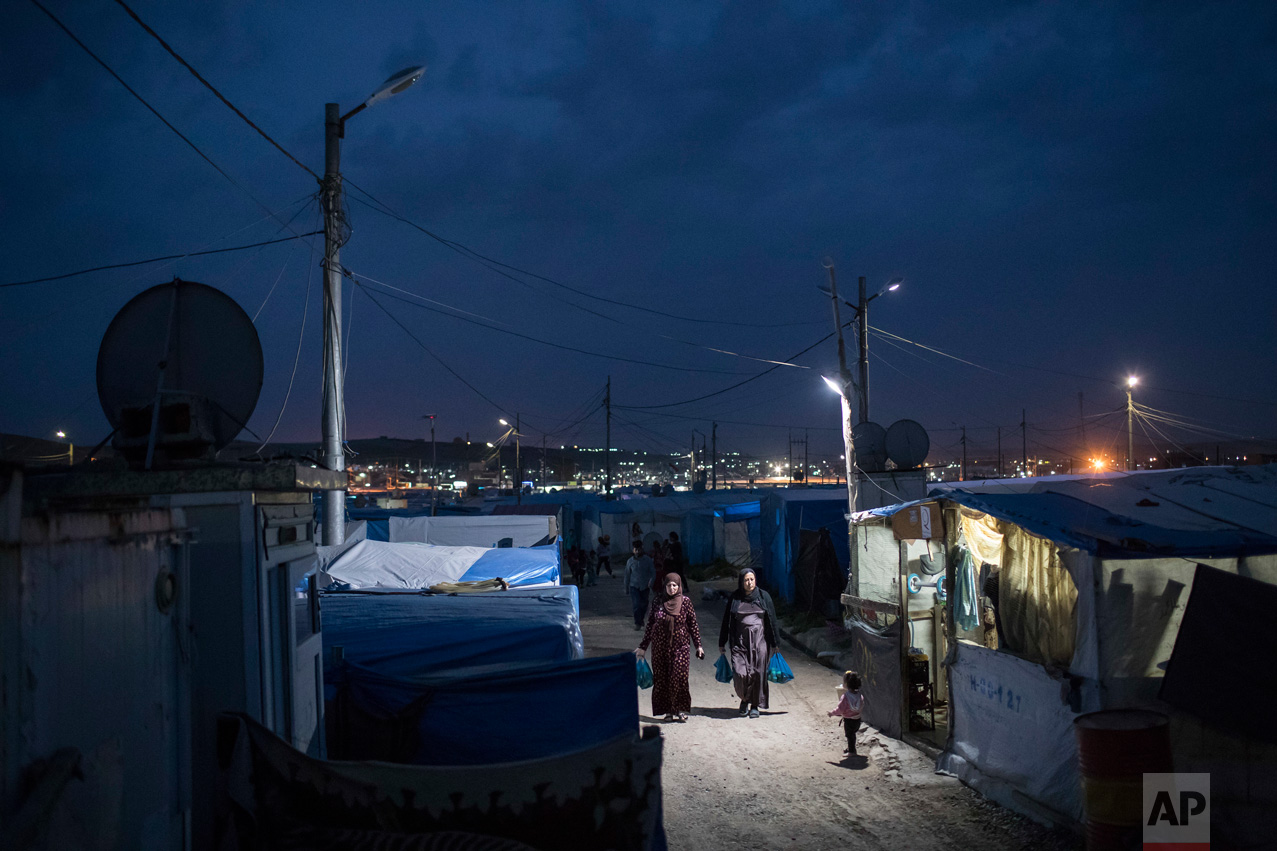 Syrian women walk through the Kawergosk refugee camp in northern Iraq, at dusk on Saturday, April 8, 2017. Millions of Syrian refugees are scattered across camps and illegal settlements across the region. (AP Photo/Felipe Dana)