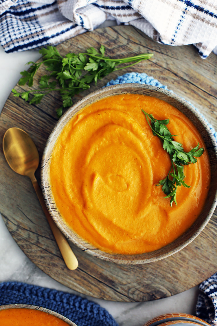 A wooden bowl full of creamy sweet potato coconut soup with a gold spoon on its side.