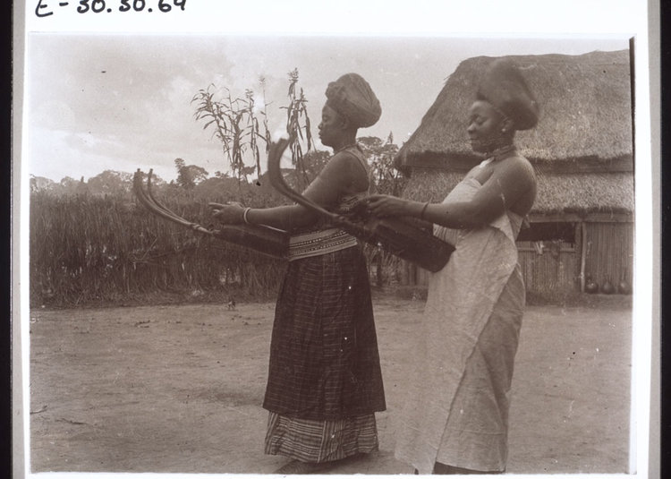 Tuke and Mowue, two of the King's wives, playing the guitar. Cameroon, 1913.
