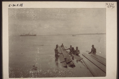 Landing boards for a Christian mission's carpentry shop in Bonaku, Douala, Cameroon, 1900. In the background, a steamer and a launch.
