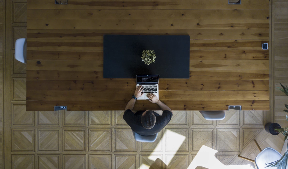 bird's-eye view of a man planning a stealth mode startup at a large wooden table