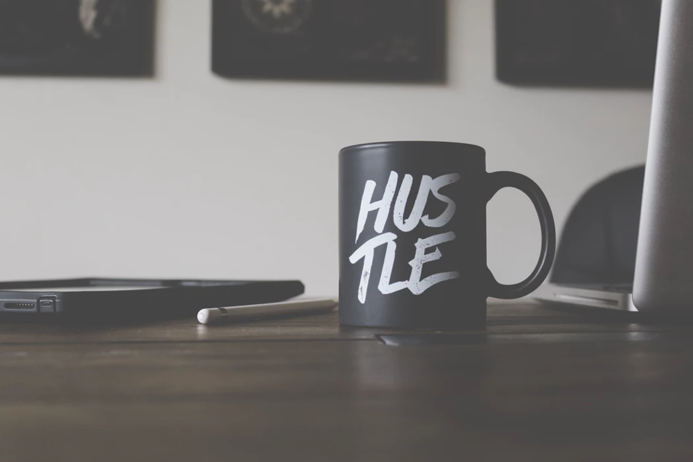 black "hustle" mug on sitting on a wooden office table on a white background