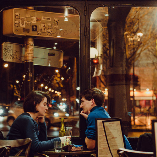 A still image of two people  sitting at a Parisian bistro having drinks.