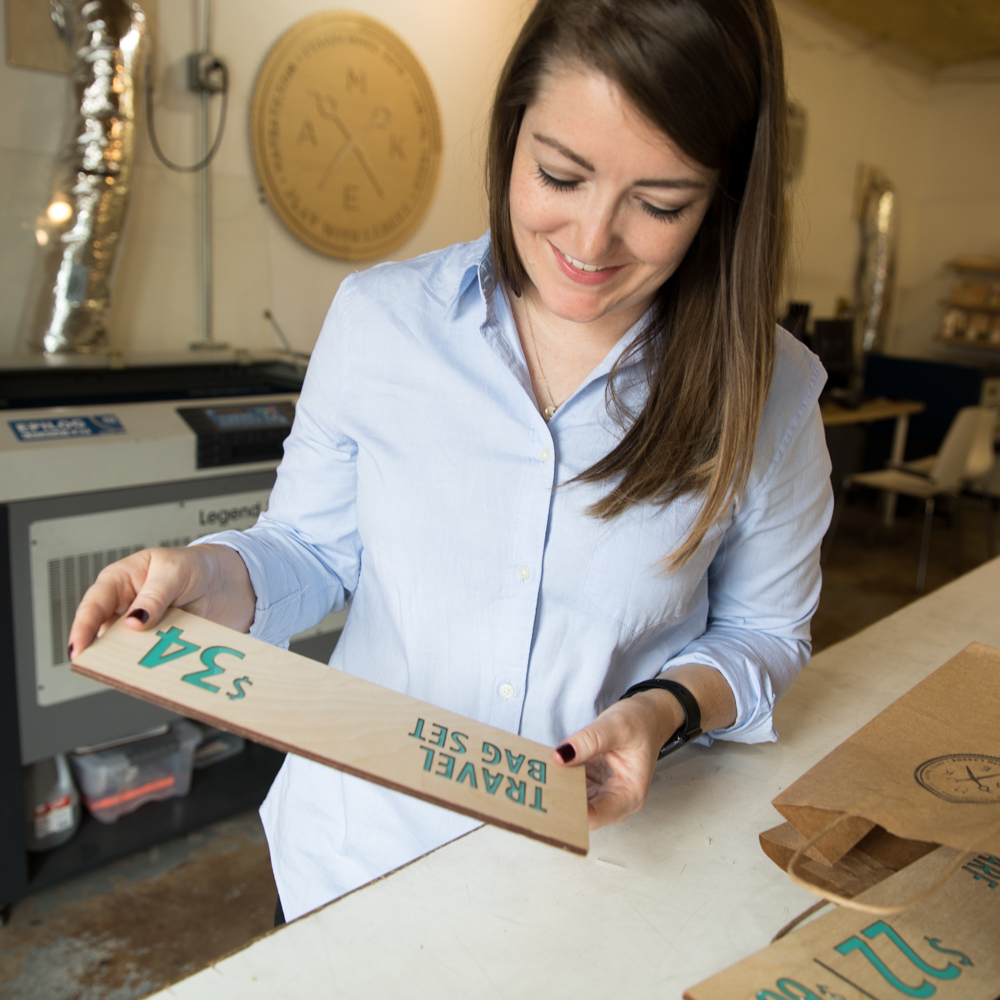 Woman holding the shop sign she just made at a laser cutting studio.