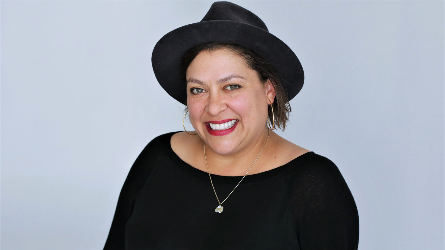 Portrait of Vinovore owner Coly Den Haan wearing a black hat and shirt, with a necklace and red lipstick
