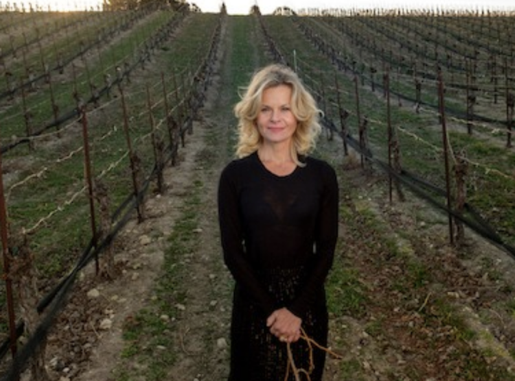 Image of a blond woman (winemaker Sonia Magdevski of Casa Dumetz) standing in a vineyard wearing black