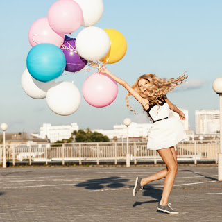 Girl laughing and holding bunch of multi-coloured balloons