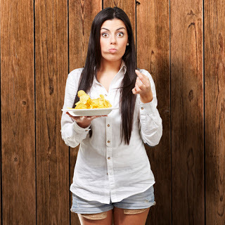 Woman holding plate of potato chips and looking guilty