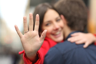 Smiling woman hugging man, holding out hand with engagement ring on it