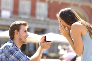 Man on bended knee, presenting engagement ring to delighted woman