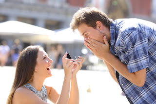 Woman on bended knee proposing to shocked man
