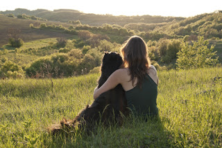 Woman cuddling dog, sitting on mountain top staring into the distance
