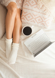 Woman on bed with coffee and laptop