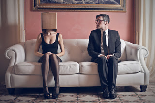 Man and woman sitting apart on sofa, woman wearing box on head