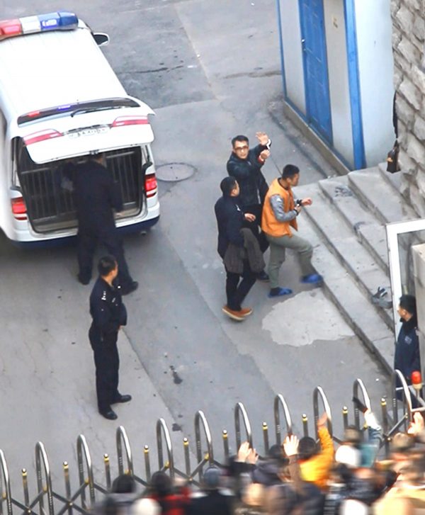 Yu Ming holds up his handcuffed hands and waves as he arrives at the court in Shenyang City on Nov. 20, 2014. (Minghui.org)