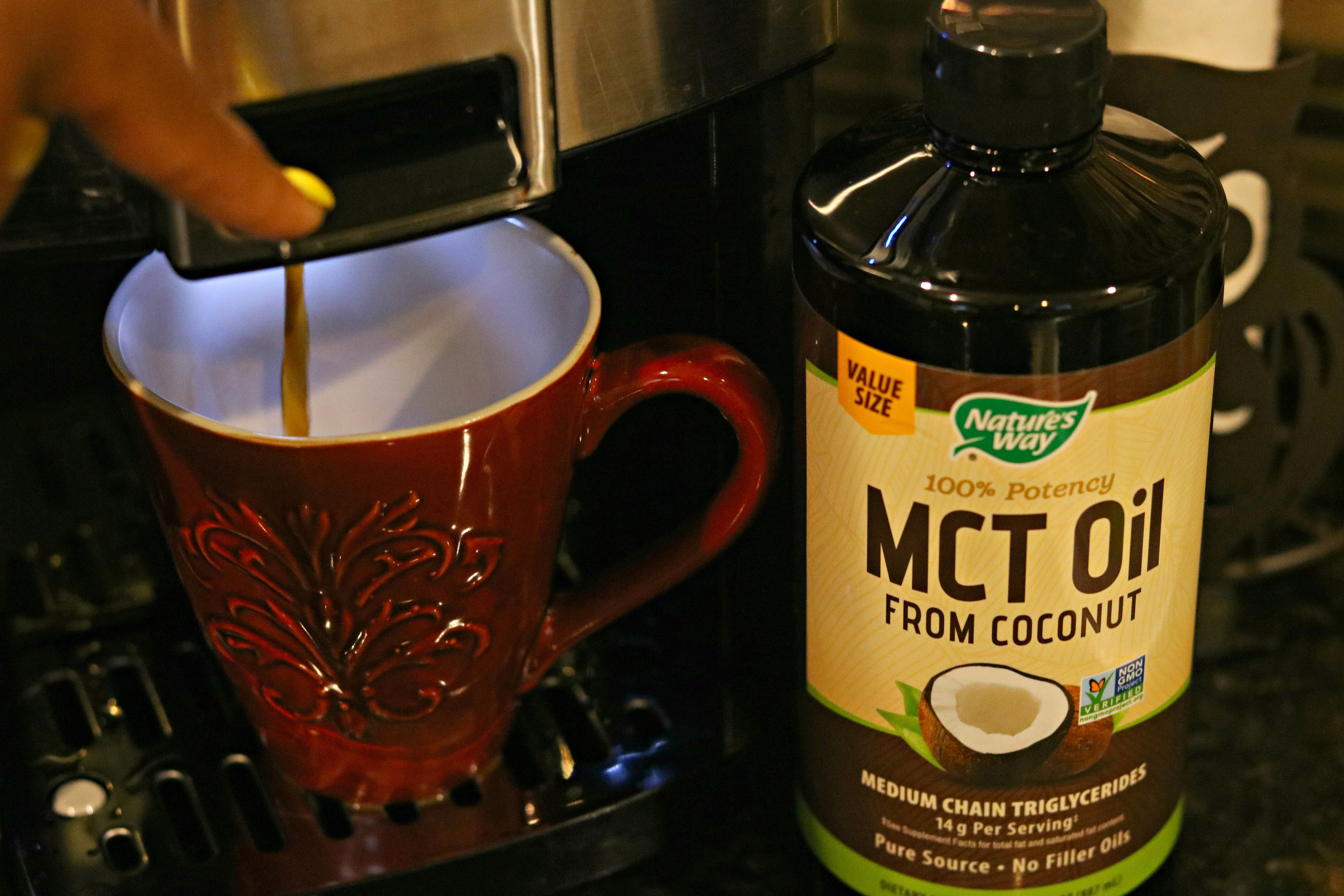 A bottle of Nature\'s Way MCT Oil next to a red mug of coffee