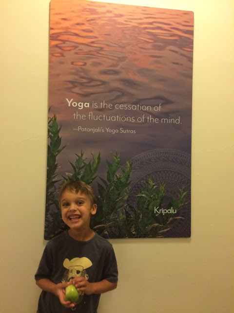 5 year old Eli smiling in front of a poster saying Yoga is the cessation of the fluctuations of the Mind