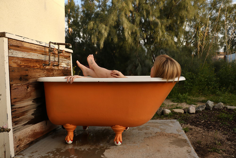 Model soaking in orange outdoor tub in Kush Queen CBD bath bomb.